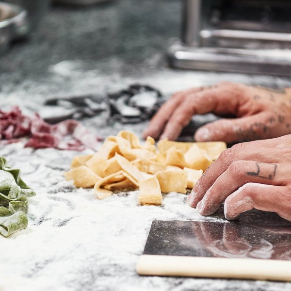 Sensoria Soulmates – Creating Memories of Bliss Tattooed hands shaping fresh colorful pasta on floured countertop