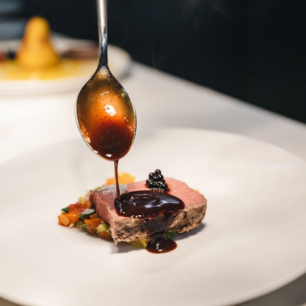 Sensoria Soulmates – Creating Memories of Bliss Sauce poured with spoon over steak on vegetables in fine dining setting