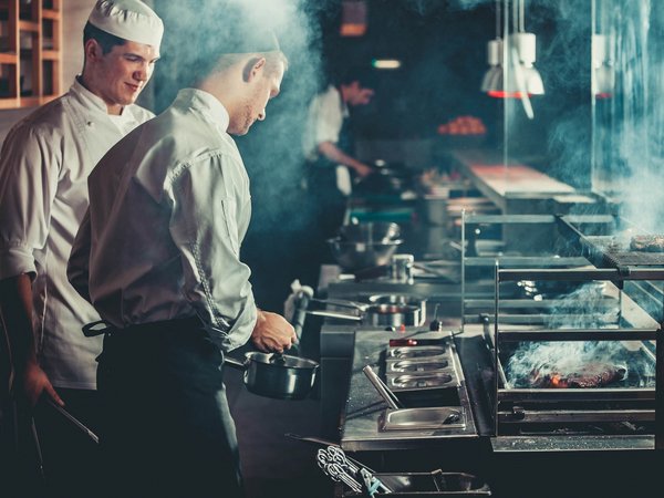 Sensoria Soulmates – Creating Memories of Bliss Zwei Köche kochen in einer rauchigen Restaurantküche am Grill und Herd