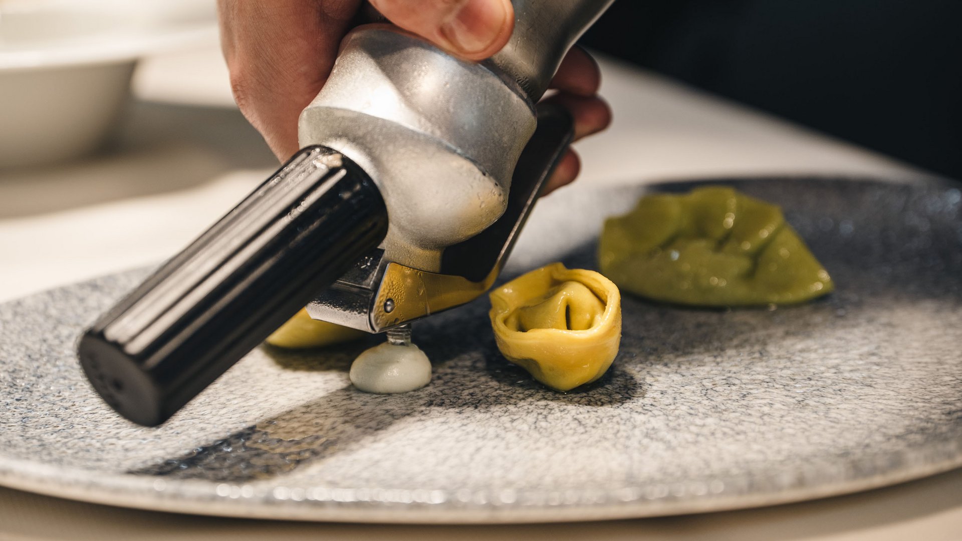 Posizioni aperte Dispenser di panna versa salsa accanto a tortellini su piatto