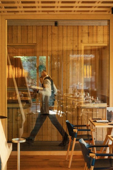 Sensoria Soulmates – Creiamo ricordi felici. Cameriere cammina nel ristorante di legno con vassoio e telefono