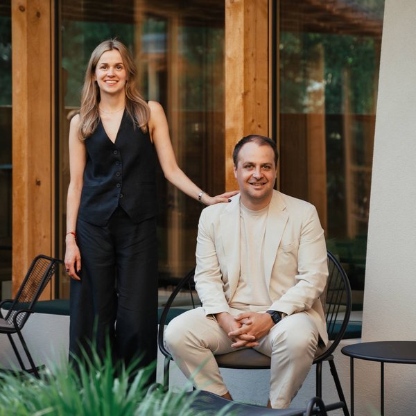 Sensoria Soulmates – Creating Memories of Bliss Woman standing and man sitting on chair in front of modern house with wooden frame