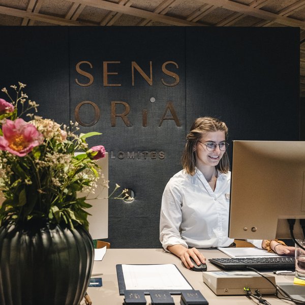 Sensoria Soulmates – Creating Memories of Bliss Woman working at computer at reception desk with flower vase in foreground