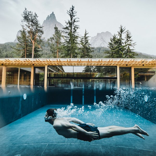 Sensoria Soulmates – Creating Memories of Bliss Person swimming underwater in pool with mountain hotel in the background